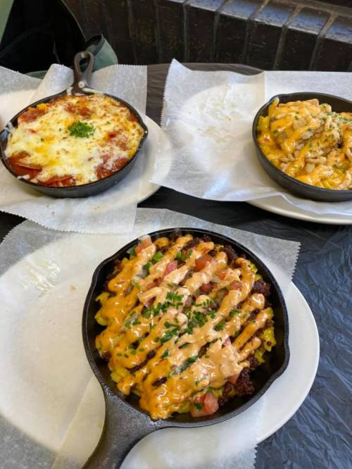 Three cast iron skillets with cheesy dishes: one with baked pasta, another with macaroni, and a third with a cheesy topping.