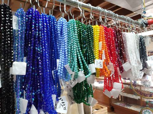 Colorful strands of beads in various shades hanging on a display, labeled with price tags.