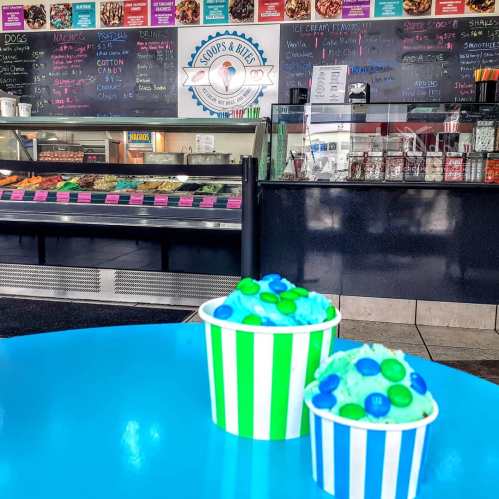 Brightly colored ice cream cups on a blue table, with a menu board and ice cream display in the background.