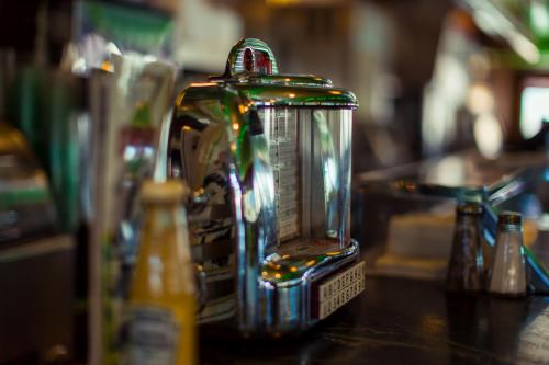 A shiny chrome jukebox sits on a bar counter, surrounded by condiments and drinks, creating a nostalgic atmosphere.