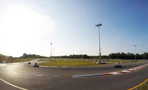 A panoramic view of a go-kart track with karts racing around a curve under a clear sky.