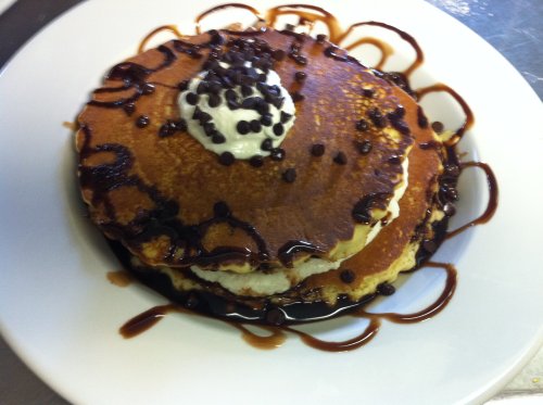 Stack of fluffy pancakes topped with whipped cream, chocolate chips, and drizzled with chocolate sauce on a white plate.