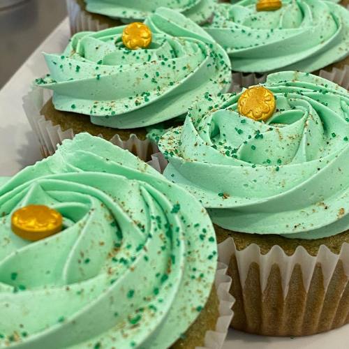 Mint green cupcakes with swirled frosting, topped with gold coins and green sprinkles, arranged on a white platter.