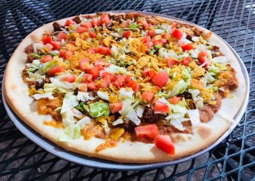 A colorful pizza topped with lettuce, tomatoes, cheese, and crunchy tortilla strips on a round crust.