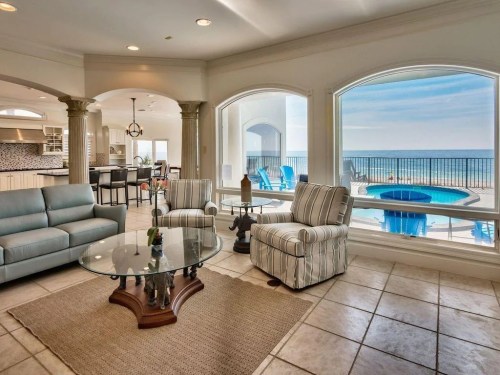 Bright living room with ocean views, featuring a glass table, striped chairs, and a cozy atmosphere.
