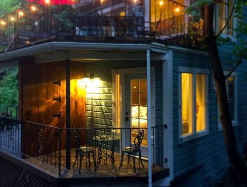 A cozy balcony with a small table and chairs, illuminated by warm light, surrounded by greenery and soft evening glow.