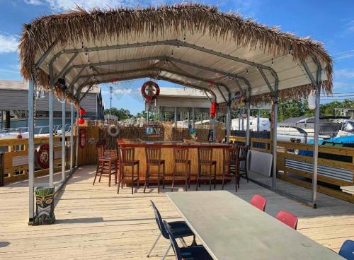 A tiki-style outdoor bar with a thatched roof, surrounded by wooden seating and boats in the background.