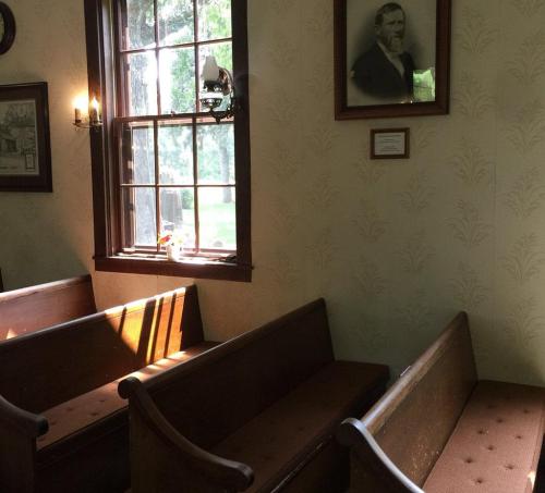 Interior of a room with wooden benches, a window letting in light, and a portrait on the wall.
