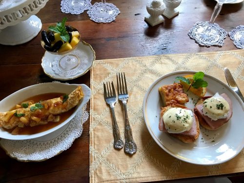 A beautifully arranged table with two plates: one with eggs Benedict and the other with a fruit dessert.