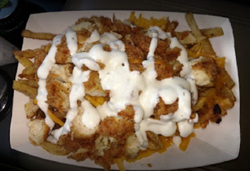 A serving of loaded fries topped with crispy chicken, cheese, and drizzled with ranch dressing.