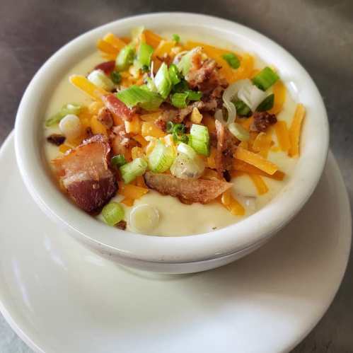 A bowl of creamy soup topped with crispy bacon, shredded cheddar cheese, and chopped green onions.