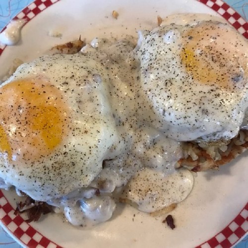 A plate of hash browns topped with two poached eggs and creamy white gravy, sprinkled with black pepper.