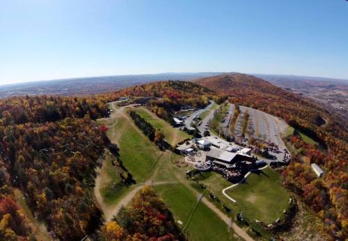 Aerial view of a mountain resort surrounded by vibrant autumn foliage and a clear blue sky.