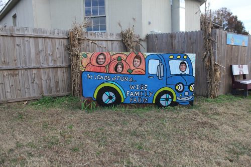 A colorful mural of a blue truck with pumpkins, featuring four cut-out faces at Wise Family Farm.