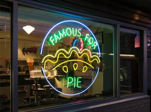 Neon sign in a window reads "Famous for Pie," with a colorful pie graphic. Inside, a diner setting is visible.