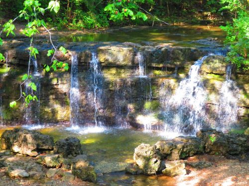 A serene waterfall cascading over rocks into a calm pool, surrounded by lush green foliage.