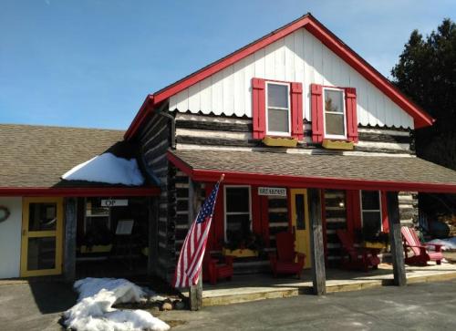 A charming log cabin-style building with red shutters, an American flag, and snow on the ground.