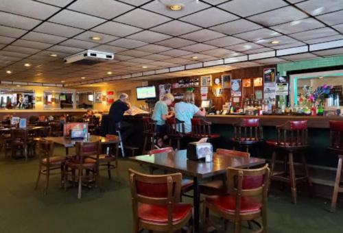 A cozy bar interior with wooden tables and chairs, a long counter, and patrons enjoying drinks in a relaxed atmosphere.
