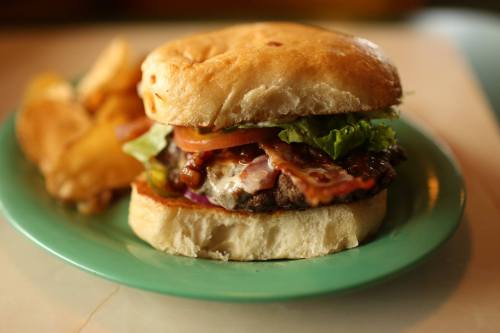A juicy burger with bacon, lettuce, tomato, and sauce, served on a soft bun with a side of potato chips.