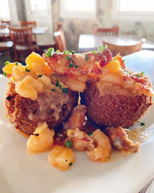 Two golden-brown fried balls topped with creamy sauce and diced ingredients, served on a white plate.