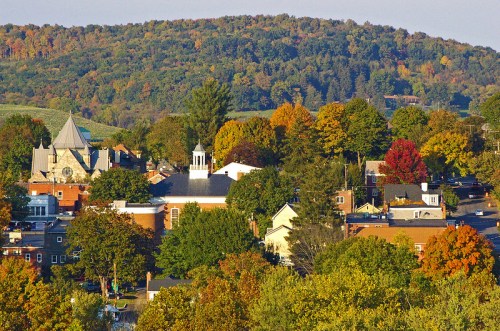 A scenic view of a small town surrounded by colorful autumn trees and rolling hills in the background.