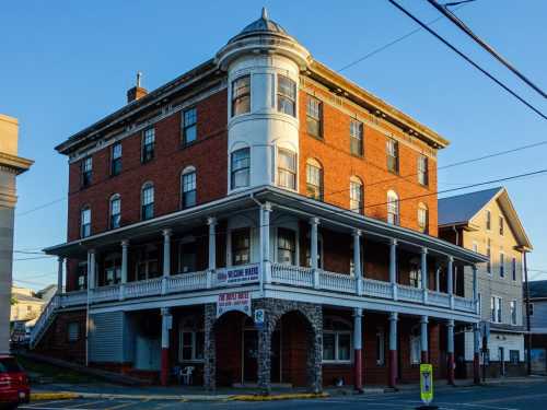 Historic brick building with a white porch, featuring large windows and a corner tower, bathed in warm evening light.