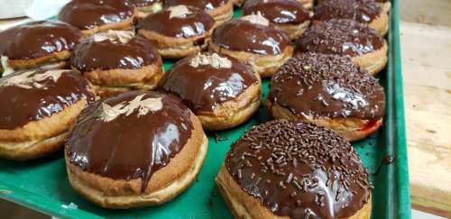 A tray of freshly baked donuts topped with chocolate glaze, some sprinkled with chocolate jimmies and others with a light decoration.