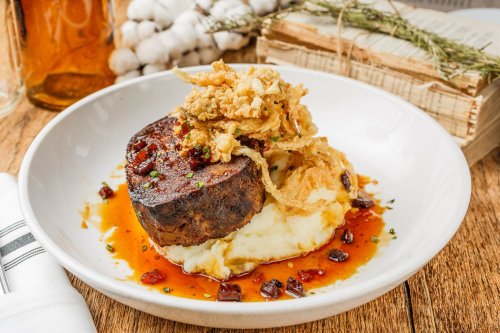 A plate of meatloaf topped with crispy onions, served on mashed potatoes with a savory sauce.