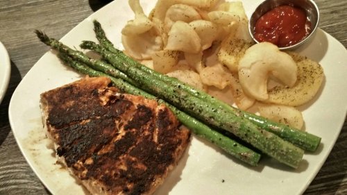 A plate with grilled salmon, green asparagus, potato chips, and a small bowl of dipping sauce.