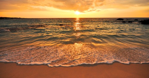 A serene beach at sunset, with golden light reflecting on gentle waves and a calm shoreline.