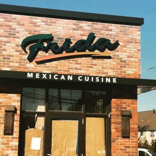 Sign for "Frida Mexican Cuisine" on a brick building with a clear blue sky in the background.