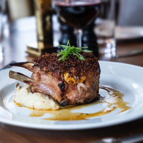 A beautifully plated pork chop with a crispy crust, served on mashed potatoes and drizzled with sauce.