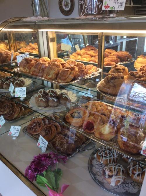 A display case filled with various pastries, including cinnamon rolls and danishes, with decorative labels and flowers.