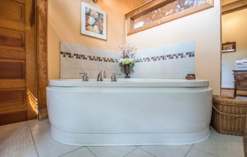 A spacious bathroom featuring a large white bathtub, tiled wall, and decorative plants in a cozy setting.