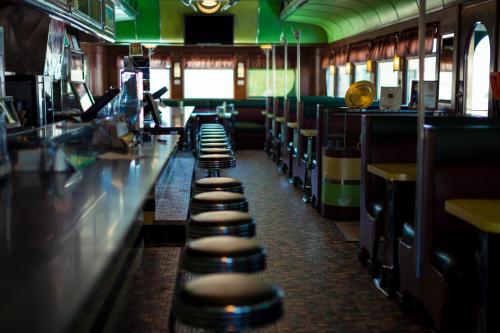 A retro diner interior featuring a long counter with stools and colorful booths, bathed in soft natural light.