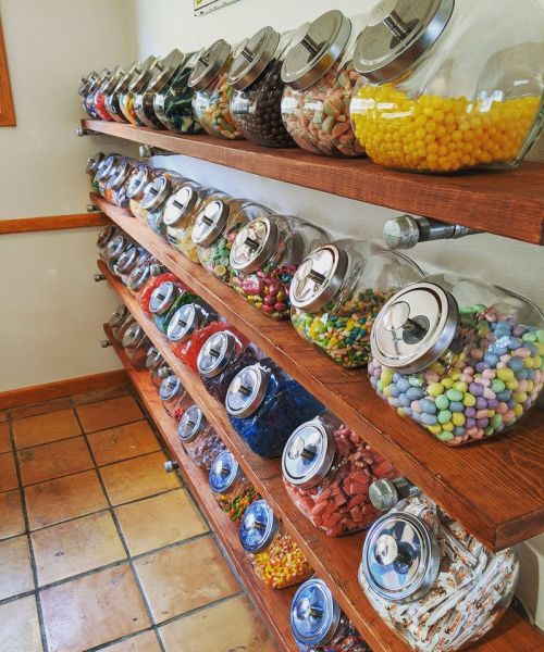 A colorful display of jars filled with various candies on wooden shelves in a shop.