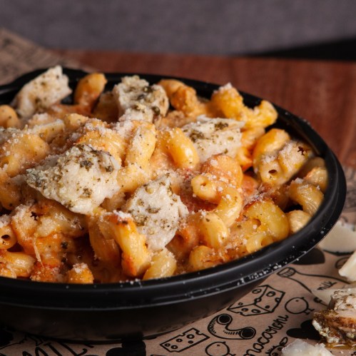 A close-up of a bowl of pasta topped with cheese and herbs, served on a patterned paper.