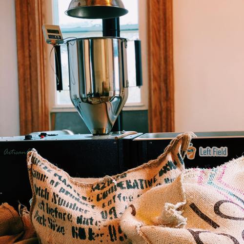 A coffee roaster with burlap sacks in a bright room, showcasing a blend of artisanal equipment and natural materials.