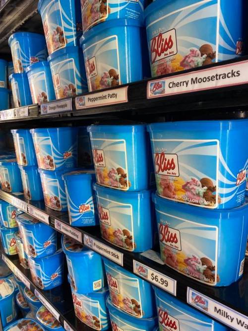 A shelf filled with colorful ice cream tubs in blue containers, featuring various flavors and prices.