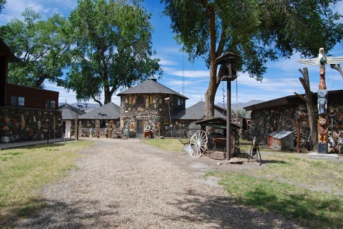 A scenic view of a stone building surrounded by trees, with a gravel path and various outdoor artifacts.