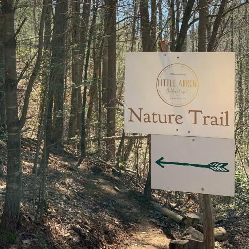 Sign for "Nature Trail" with an arrow pointing left, surrounded by trees in a wooded area.