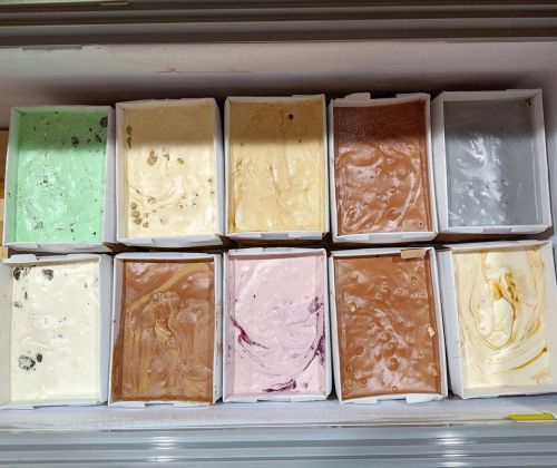 A variety of ice cream flavors in rectangular containers, arranged in two rows, showcasing different colors and textures.