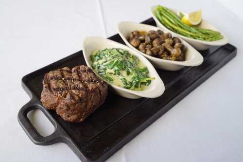 A gourmet meal featuring a grilled steak, creamy spinach, sautéed mushrooms, and asparagus on a serving platter.