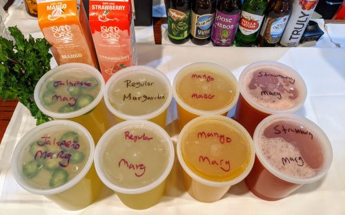 Eight labeled containers of colorful drinks, including jalapeño margarita, regular margarita, and mango and strawberry mixes.
