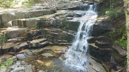 A serene waterfall cascading over rocky terrain, surrounded by lush greenery and sunlight filtering through the trees.