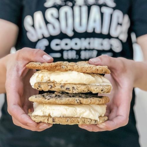 A person holds a towering ice cream sandwich made with three large cookies and a scoop of ice cream in the center.