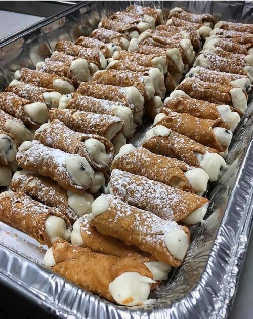 A tray filled with neatly arranged cannoli, dusted with powdered sugar and filled with creamy filling.