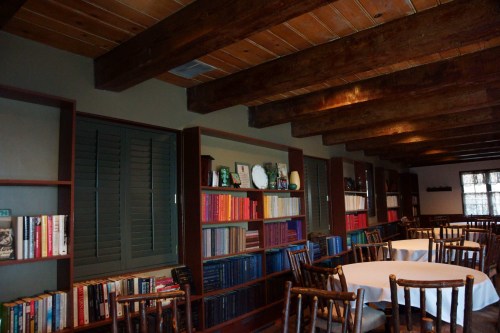 Cozy interior with wooden beams, bookshelves filled with books, and tables set for dining.