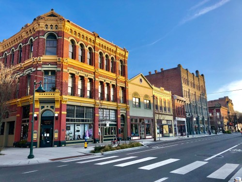 Historic buildings line a street under a clear blue sky, showcasing vibrant architecture and a charming urban atmosphere.