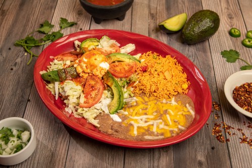 A vibrant plate of Mexican food featuring rice, beans, grilled vegetables, lettuce, and sliced avocado on a wooden table.